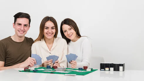 Trzy uśmiechnięte osoby siedzą przy stole i grają w grę karcianą z żetonami pokerowymi. Atmosfera jest relaksująca i wesoła, przypominająca przyjemny wieczór gier.